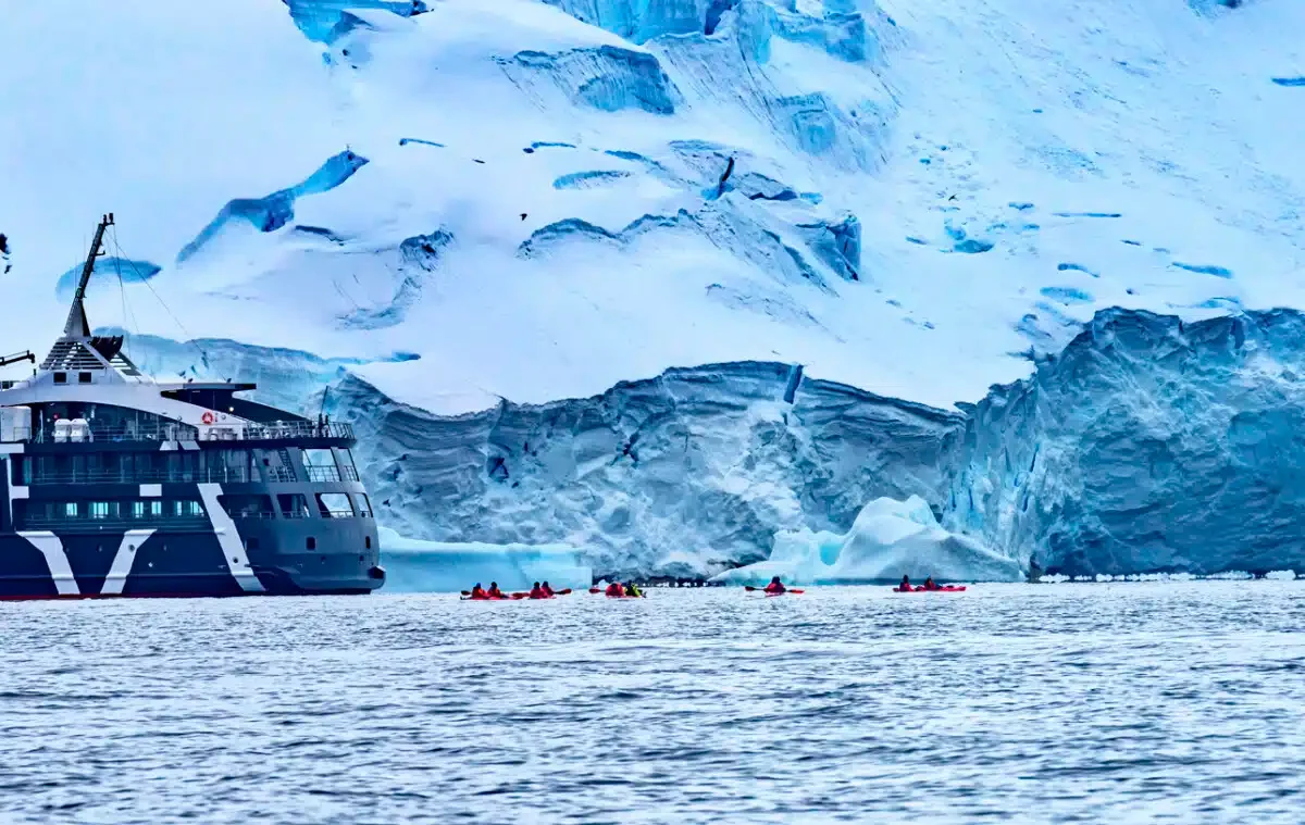 Ship Red Kayaks Tourists Glaciers Snow Mountans Charlotte Bay Antarctic Peninsula Antarctica. Glacier ice blue because air squeezed out of snow.
