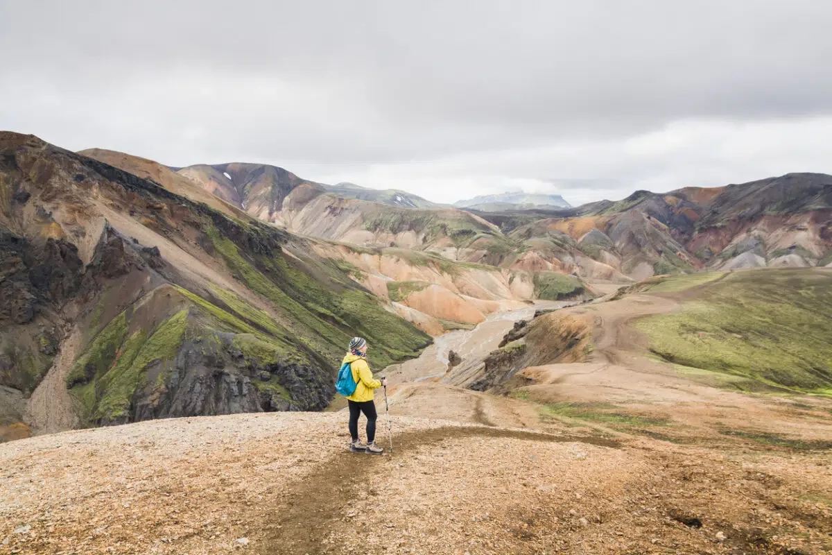 Woman in yellow raincoat hiking uphill in the colourful mountains in Landmannalaugar national park, Iceland.