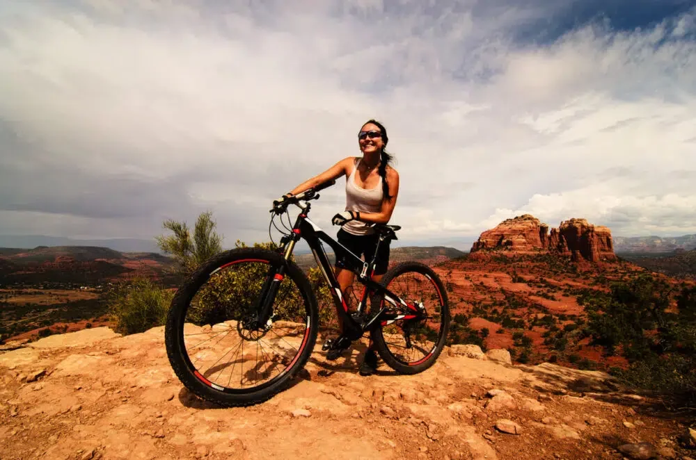 Happy young girl standing on the cliff with her bike and beautiful panorama of desert in USA behind.