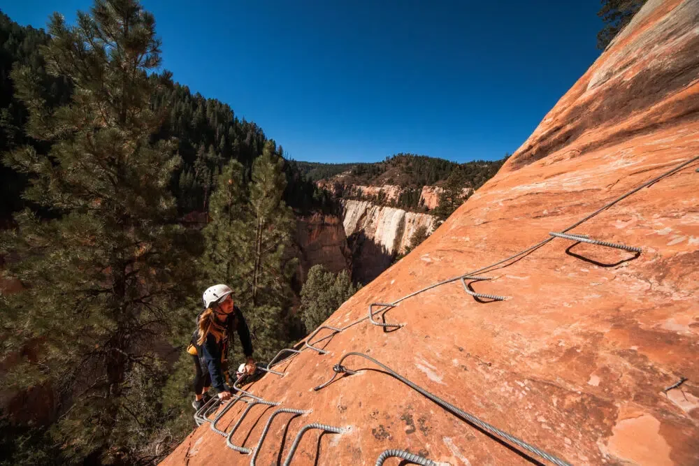 A climber using a ladder and ropes to scale a boulder