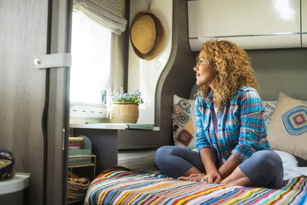 Woman and relax indoor leisure activity alone. One female people sitting on bedroom inside camper van and looking outside the window. Travel and serene happy lifestyle people. Healthy mindful vanlife